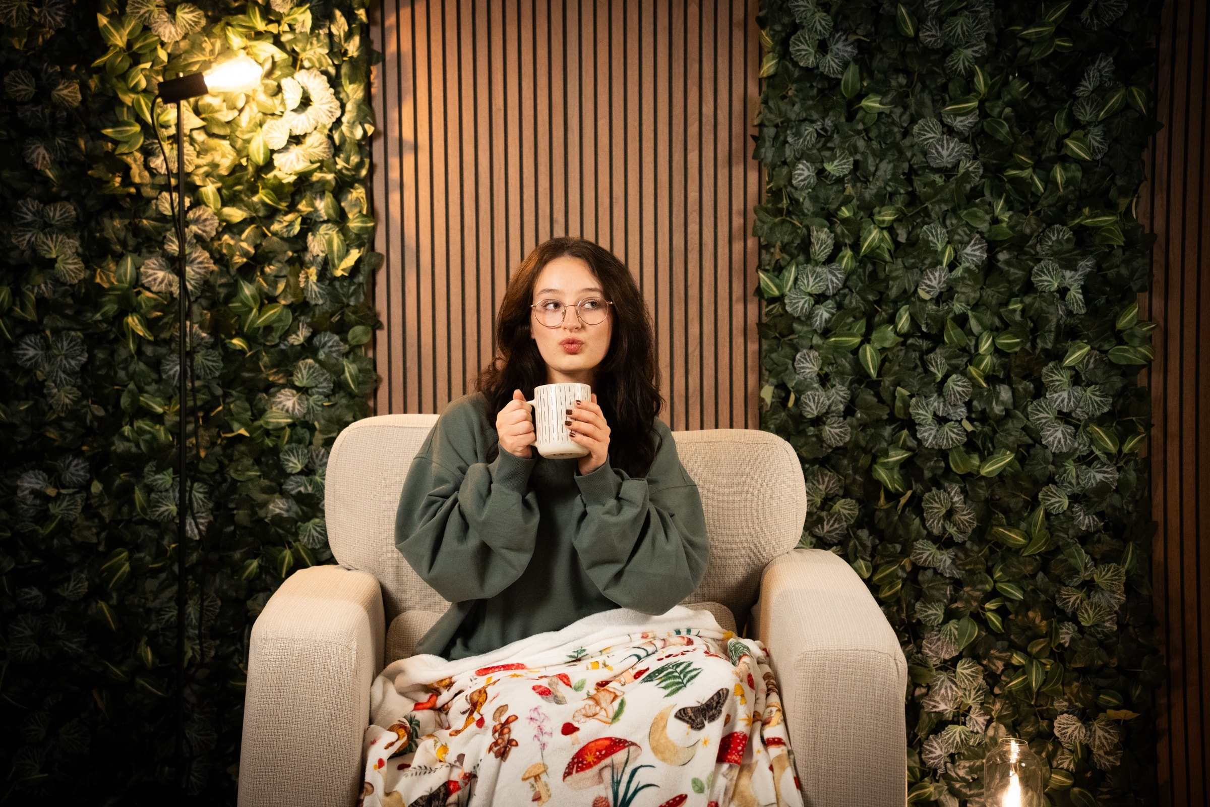 Kare with a mug, wrapped in a blanket in the room where the podcast is recorded
